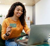 Woman sitting at laptop, smiling holding credit card