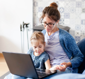 Woman with glasses sitting with her child looking at a laptop reviewing credit union credit cards