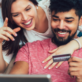 Woman and man smiling looking at credit card and laptop