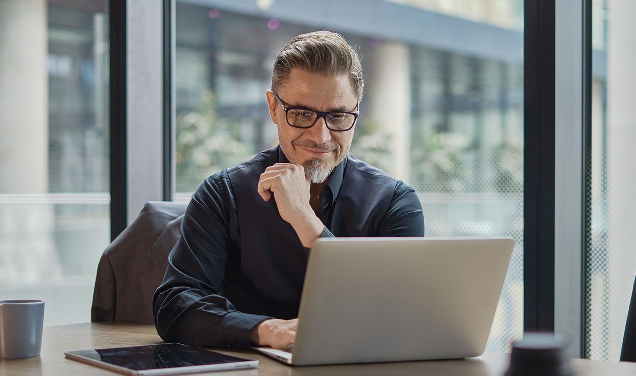 Business professional wearing glasses sits at a desk using a laptop