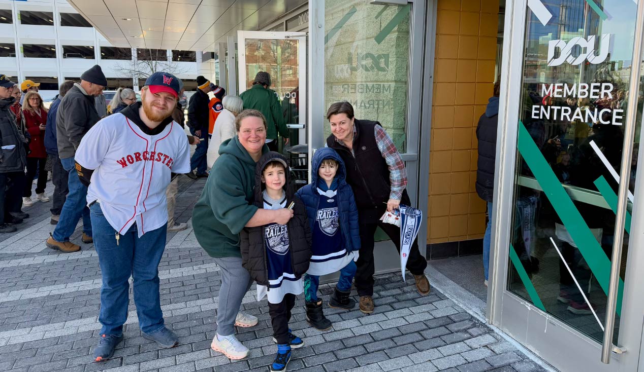 A smiling family standing outside of DCU Center Member Entrance.