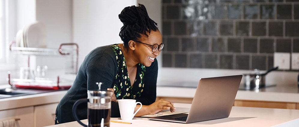 Woman leaning on the counter looking at her laptop and smiling