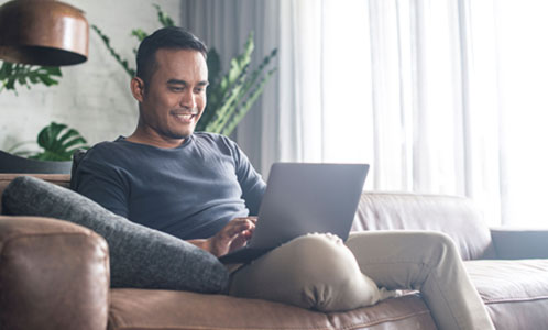 Man sitting on the couch looking at his laptop and smiling
