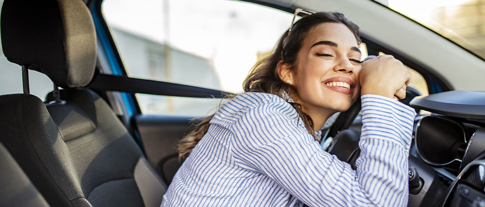 Woman in the driver's seat leaning forward onto steering wheel and smiling