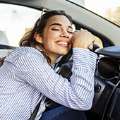 Woman smiling leaning on steering wheel inside car