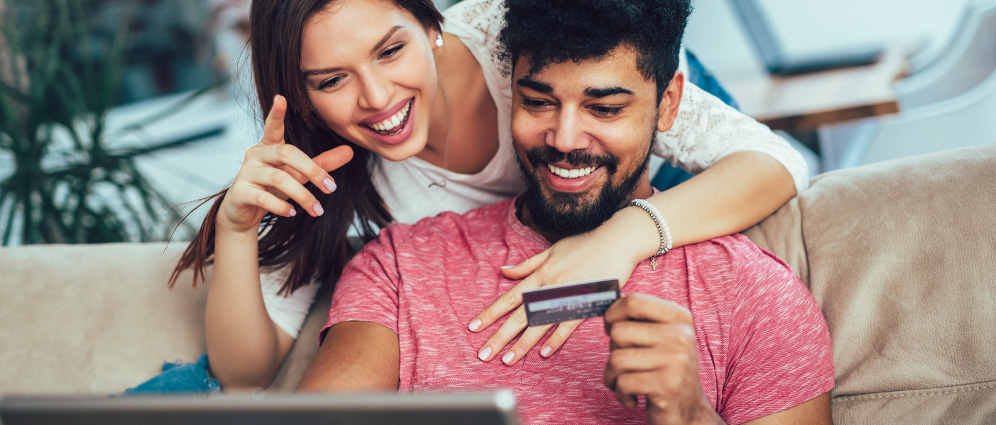 Couple smiling and holding a credit card while shopping online