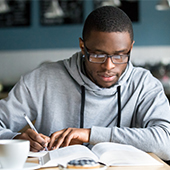 Young man with open book, studying and taking notes.