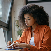 Young woman writing notes while staring at computer