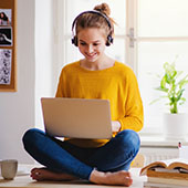 Student sitting cross-legged while working on their laptop with headphones on