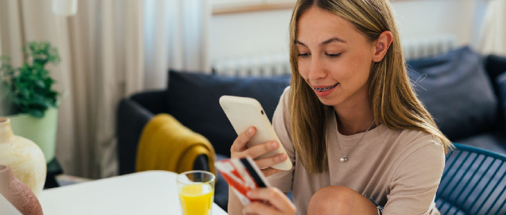 young woman looking at phone while holding a credit card in hand