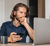 Serious man looking at computer, factoring the impact of his credit score on buying a car