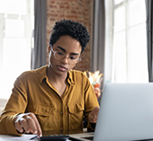 Woman with glasses, sitting at computer calculating fees associated with bank account transactions