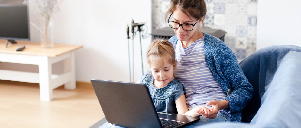 Smiling woman sitting holding her child's hand and looking at laptop