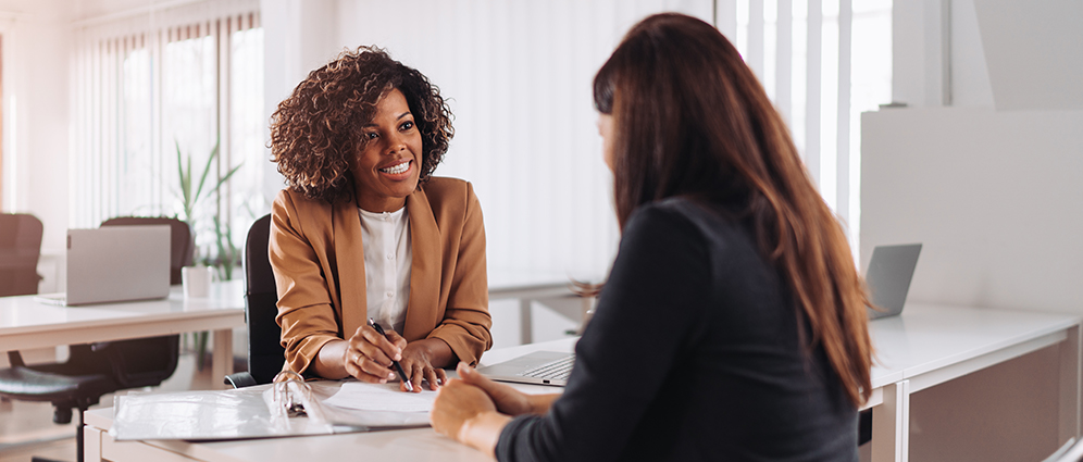 Two women seated at a desk going over a contract. 