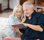 Older man and woman, lounging, looking at digital banking on a tablet