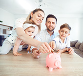 Young family sitting down and adding money into a piggy bank