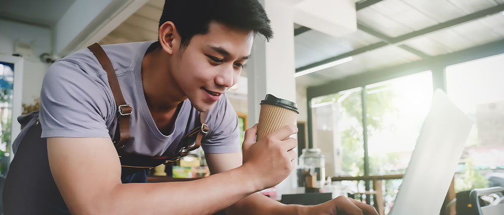 Young man bent over his computer while holding a cup of coffee