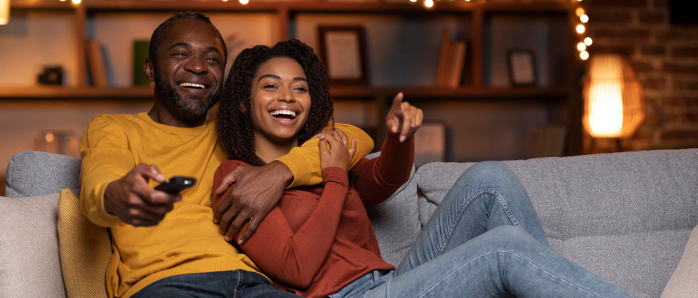 Couple sitting on a couch laughing at tv together
