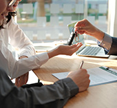 Man and woman sitting at desk, signing documents for a car loan and getting the keys