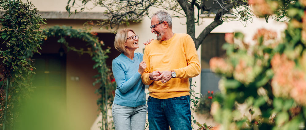 Retirement age couple standing in garden, smiling at each other