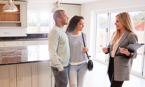 happy couple in kitchen speaking to a friendly female realtor