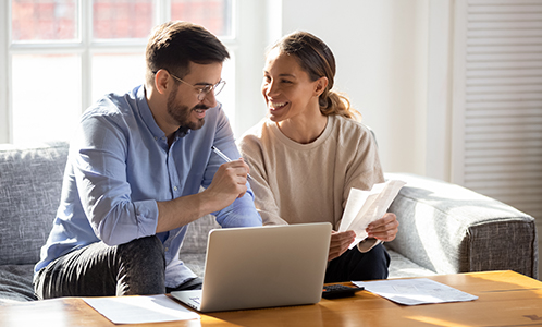 couple smiling looking at paperwork and laptop