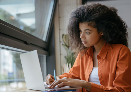 Young woman writing notes while staring at computer