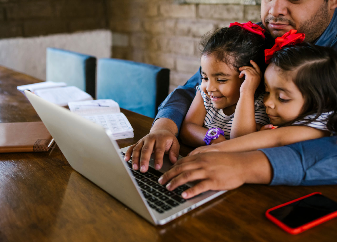 Man with toddlers on his lap looking at laptop