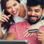 Man and woman smiling, holding a store credit card looking at a laptop