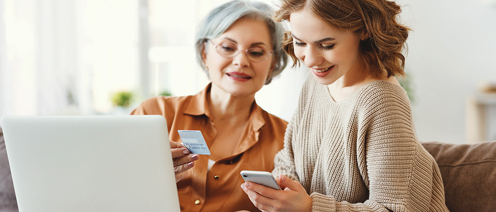 Two women smiling looking at a subscription card and phone