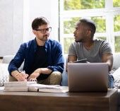 Two people sitting on a couch, talking in front of a laptop