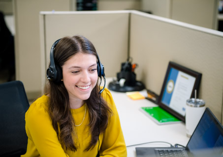DCU Employee smiling at computer and wearing a headset.