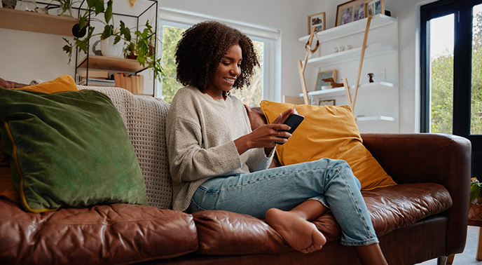 woman sitting on a sofa holding her phone and smiling