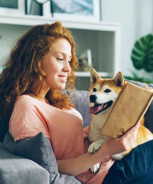 Woman reading on couch with happy dog beside her.