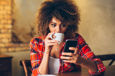 A young woman drinking coffee and browsing her mobile phone