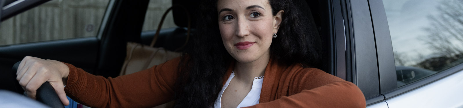 Woman sitting in drivers seat of her car and smiling.