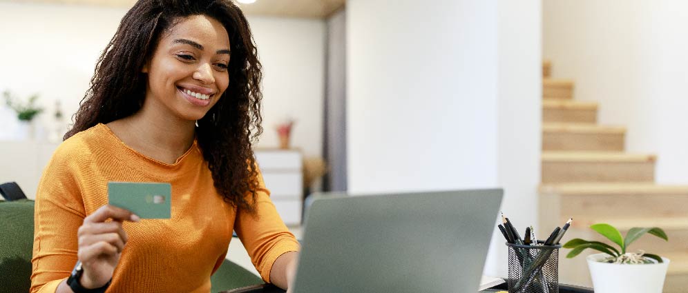 Smiling woman holding credit card in one hand and operating laptop with the other.