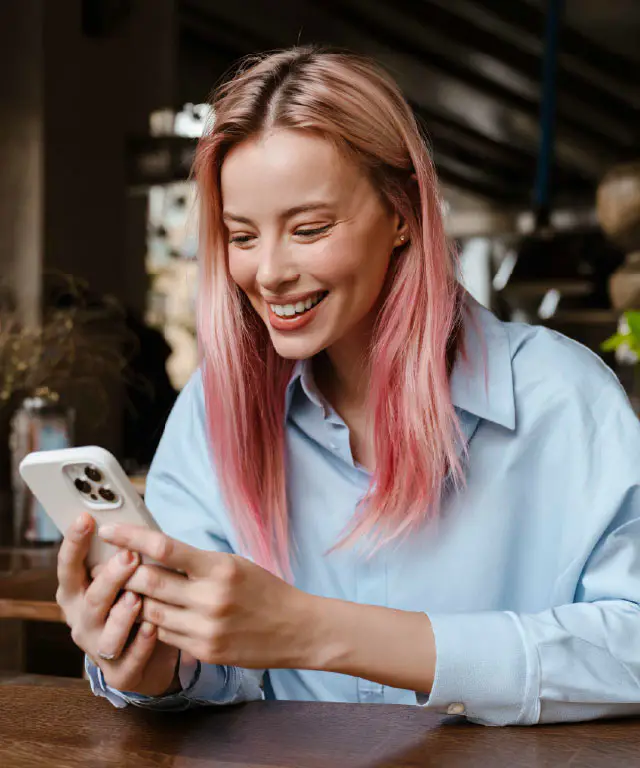A woman smiling and looking at her phone while sitting indoors.