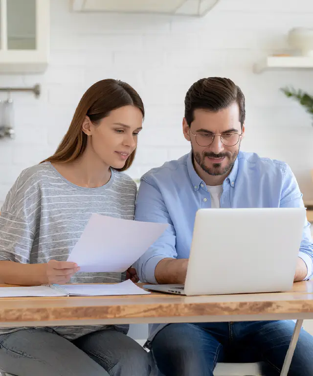 Two people sitting at a table, reviewing documents and using a laptop