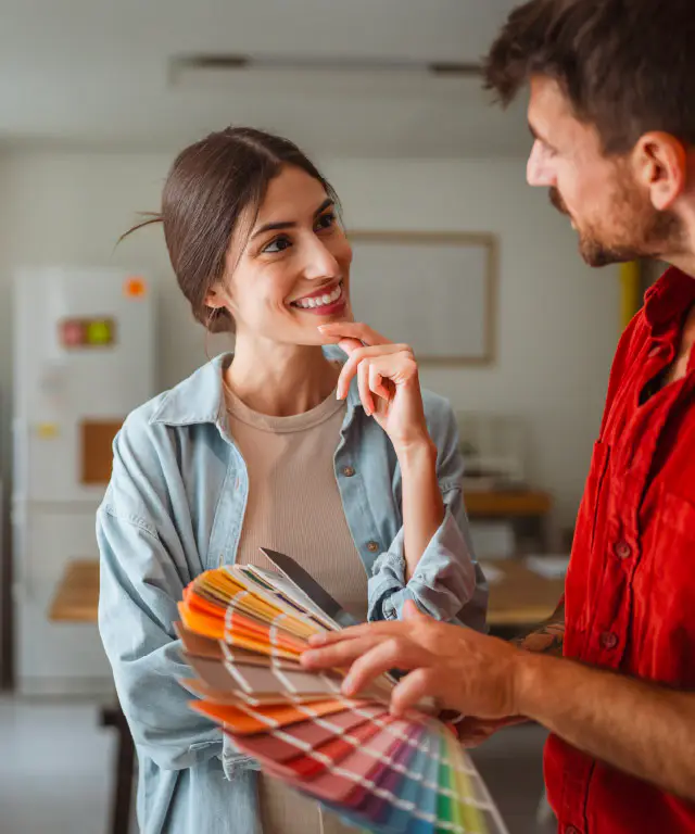 Two people stand indoors reviewing color samples and discussing options.