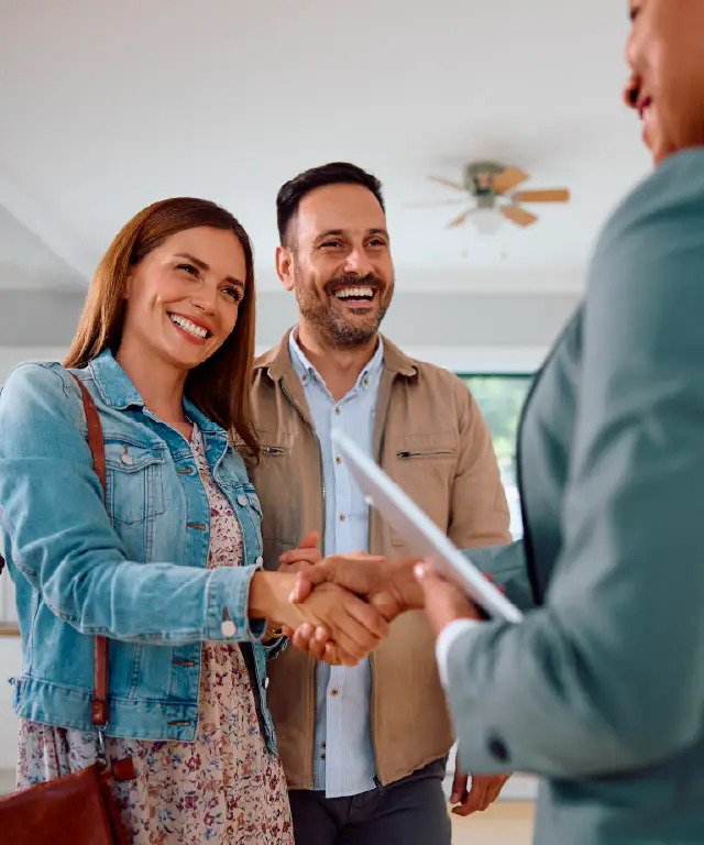 Three people stand indoors as one person hands a document to another.