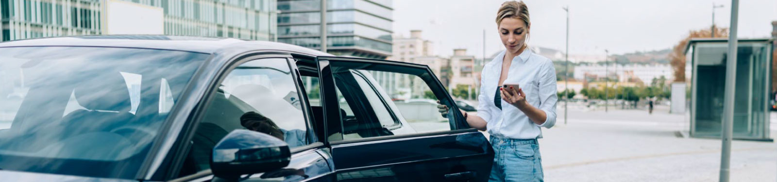 Woman standing in front of an opened car door and looking at her phone.