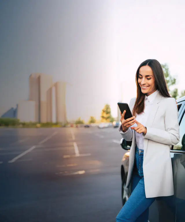 Woman leaning against her car and smiling at something on her phone