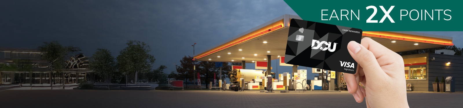 Hand holding DCU Visa card in front of a gas station