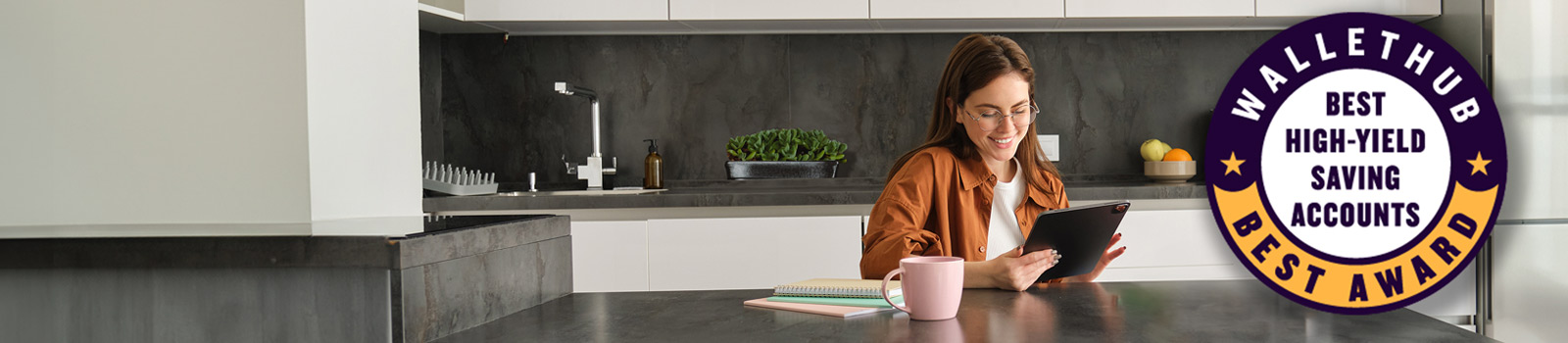 Woman sitting at a counter smiling at something on the tablet she is holding.