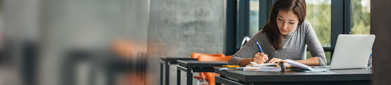 a young female student in a classroom sitting by the window and taking notes