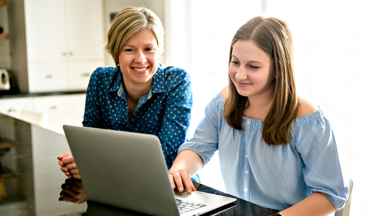 25-BRDVAL-4839 Greenlight Hero and Inline A mother and daughter sitting at the counter while smiling at something on a laptop.
