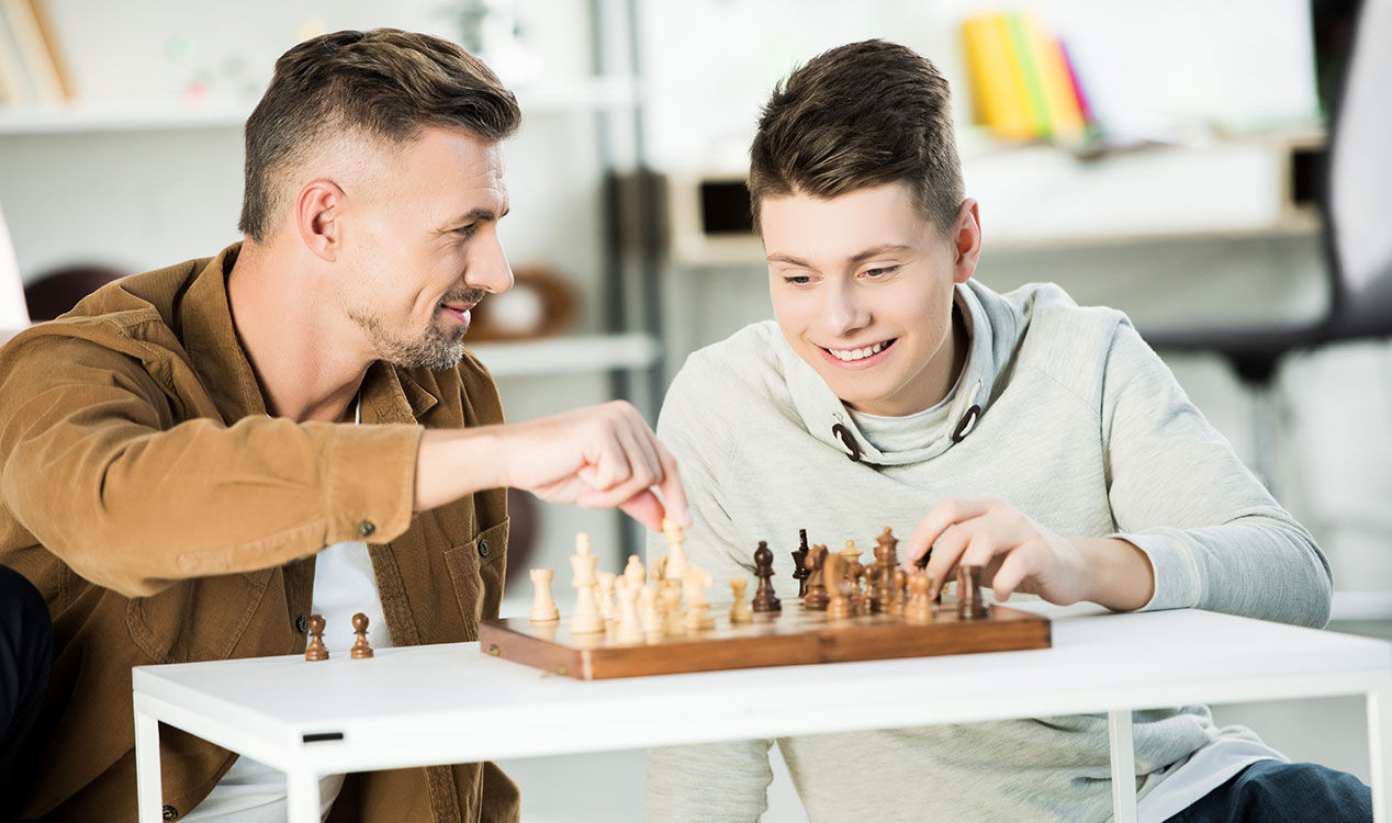 A father and son seated at a table and playing Chess
