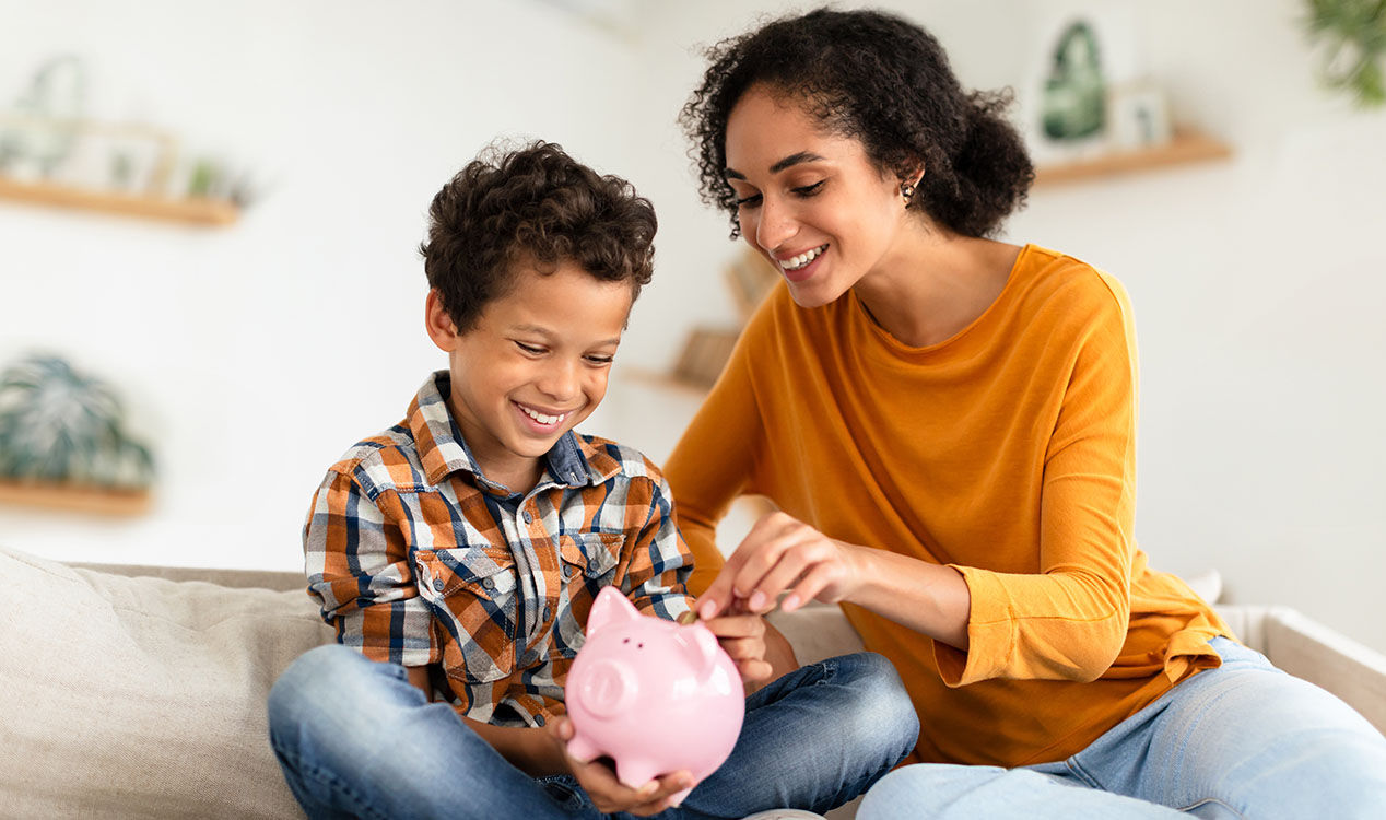 A mother smiling beside a child holding a piggy bank