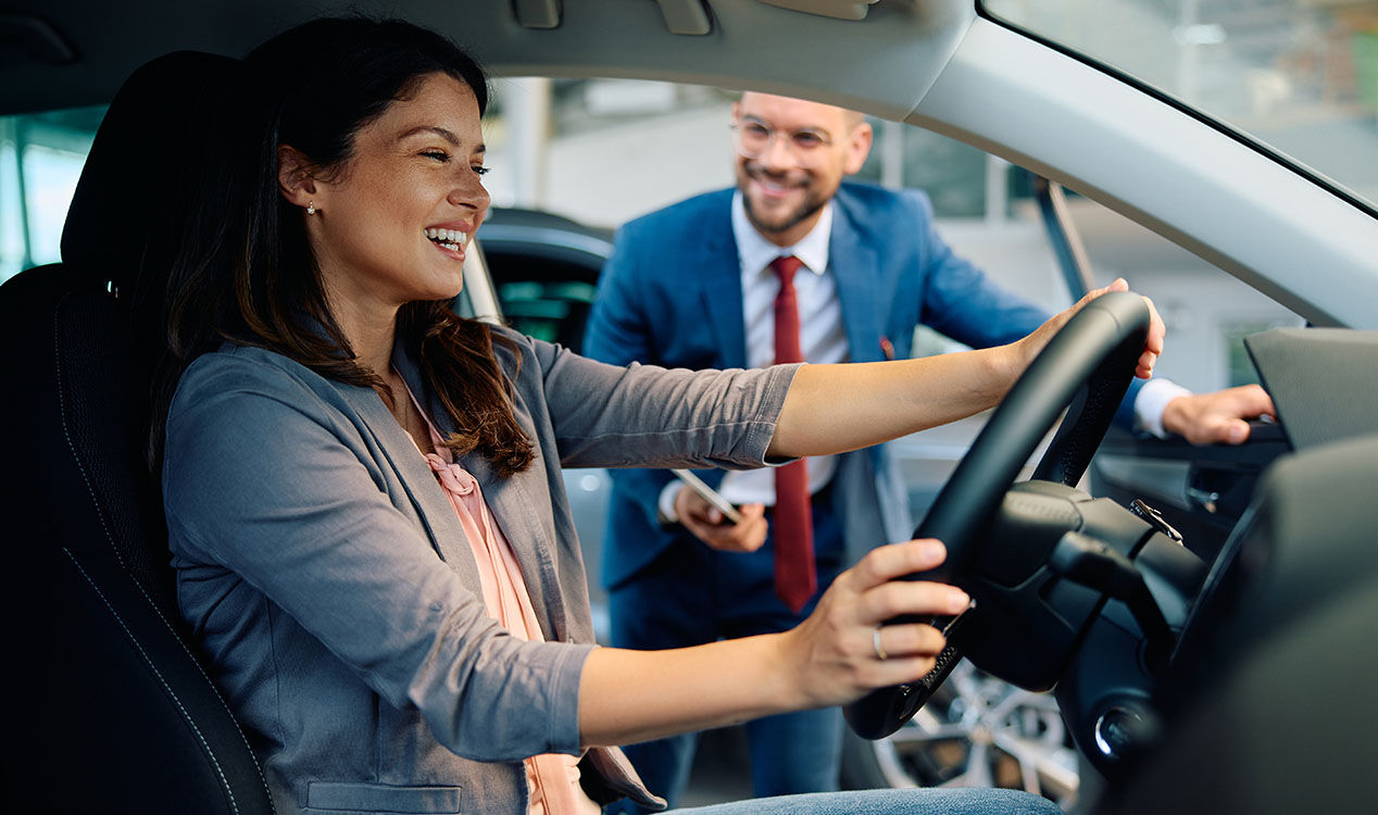 a woman at the steering wheel with a man standing outside the car